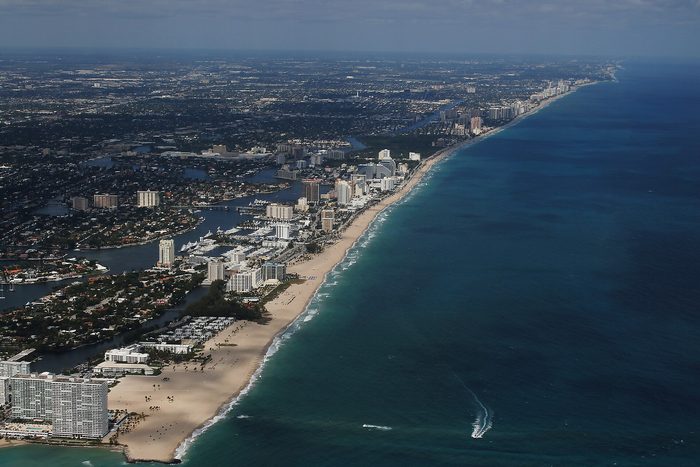 Aerial view of a long beach lined with high-rise towers, the ocean on the right.