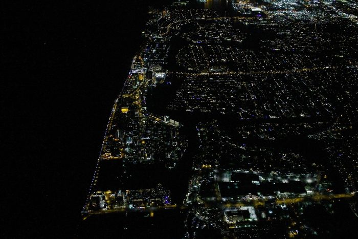 Night aerial of the beach strip, with lit streets and towers along the dark ocean.