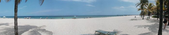 Wide panorama of white sand, blue water and a few beachgoers.