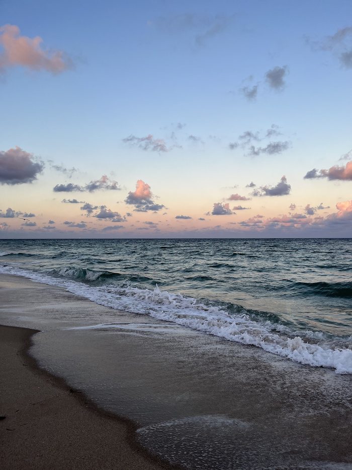 Low waves rolling onto the sand under a pink and blue evening sky.