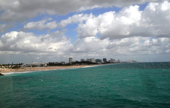 Turquoise water and a long beach curving toward a row of distant towers under puffy clouds.