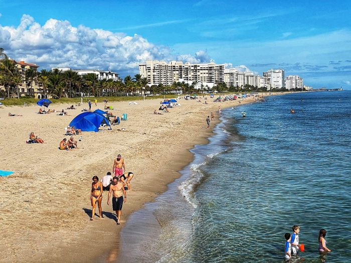 Beachgoers on the sand at Lauderdale-by-the-Sea, with condominium towers along the shore in the distance.